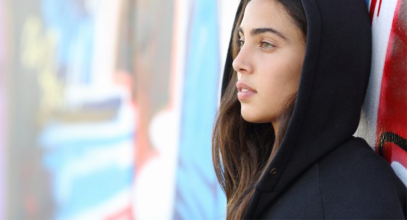 Teenage girl hood up leaning against wall