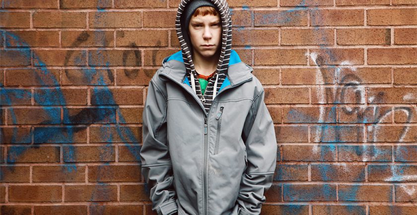 Teenage boy wearing grey jacket and striped hood standing against wall Teenage boy wearing grey jacket and striped hood standing against wall