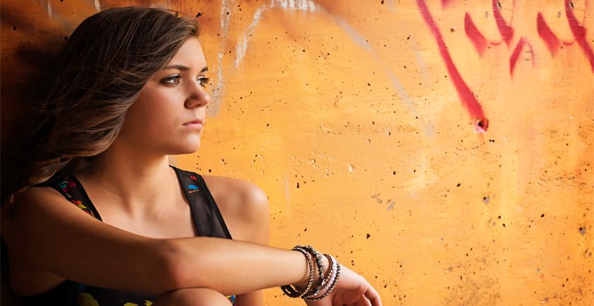 Teenage girl sitting against orange wall