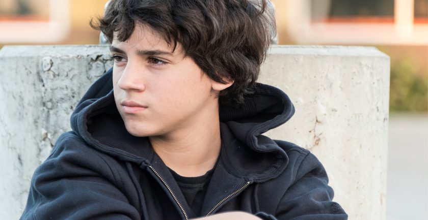 Dark haired teenage boy sitting against wall