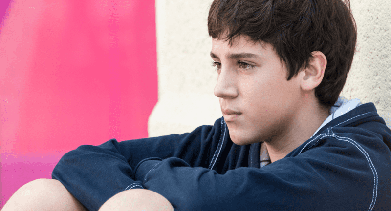 Dark haired boy in navy top sitting against wall