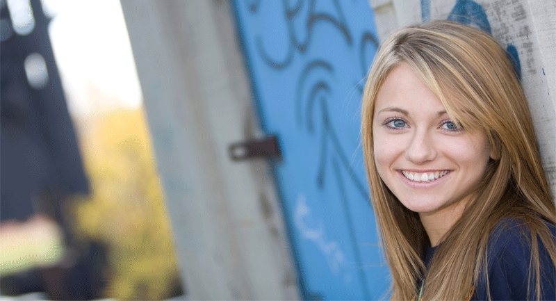 Teenage girl with long fair hair standing against wall