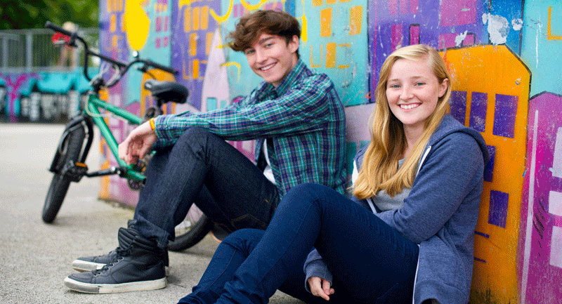 teen-girl-and-boy-sitting-against-a-graffitti-wall