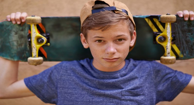 Teenage boy holding skateboard on shoulders