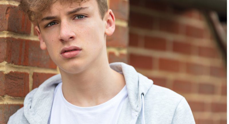 boy-teenager-outside-leaning-on-brick-wall-wearing