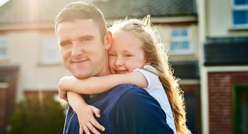 Young girl holding onto father around his shoulders Young girl holding onto father around his shoulders