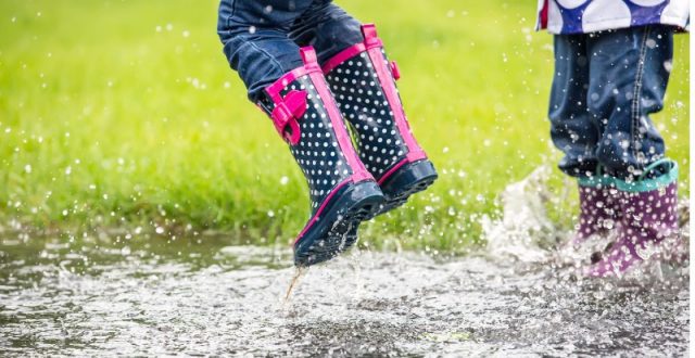Two girls with welly boots on jumping into a big puddle