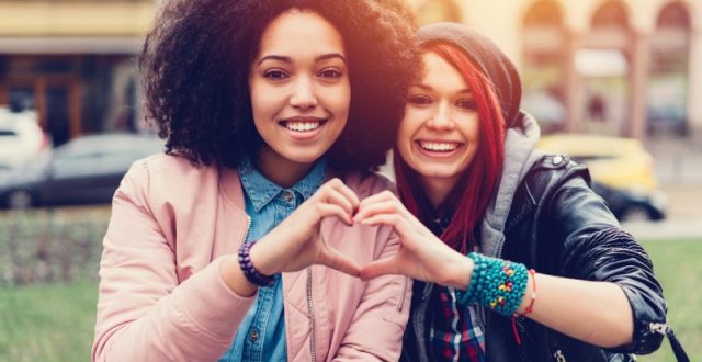 Two young women friends makinig a heart shaped gesture with their hands