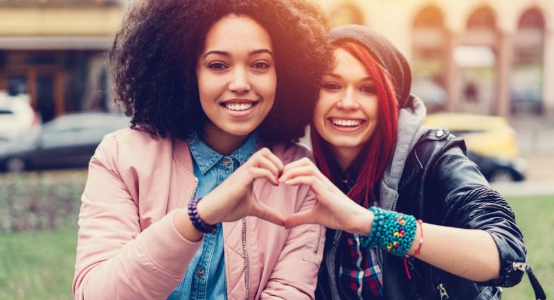 Two young women friends makinig a heart shaped gesture with their hands