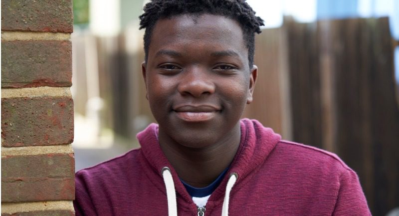 portrait-of-smiling-teenage-boy-leaning-against-wall-in-urban-setting