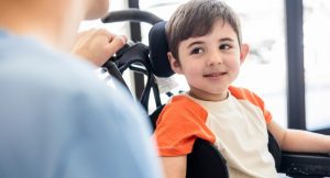 beautiful-little-boy-on-wheelchair-smiling-and-looking-with-at-his-picture-id1055956092