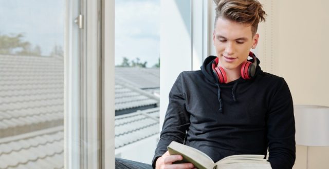 Teenage boy reading a book by a window