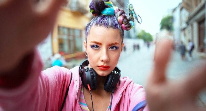 Girl with multi-coloured hair and a pink jacket with headphone round her neck