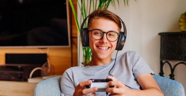 Smiling teenage boy playing a console with headphones on
