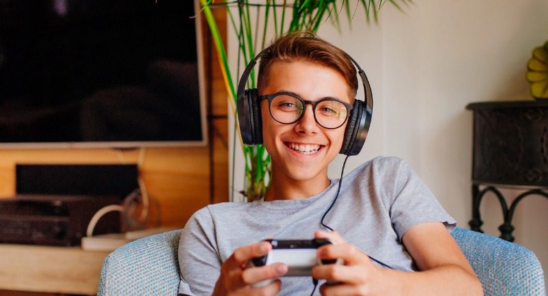 Smiling teenage boy playing a console with headphones on