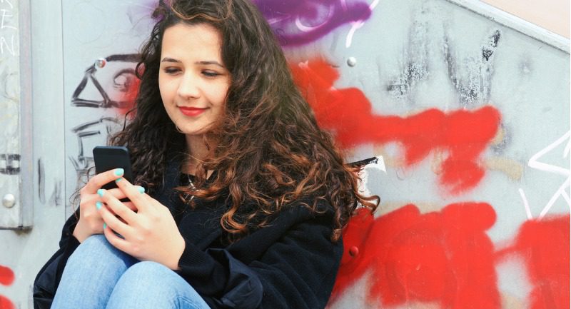 Young woman sitting in front a graffiti wall using her phone