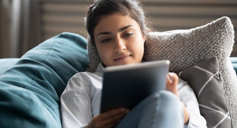 young-indian-woman-rest-on-sofa-watching-movie-on-tablet