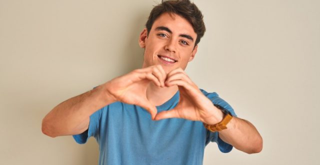 Teenage boy wearing a blue t-shirt making a heart shape with his hands