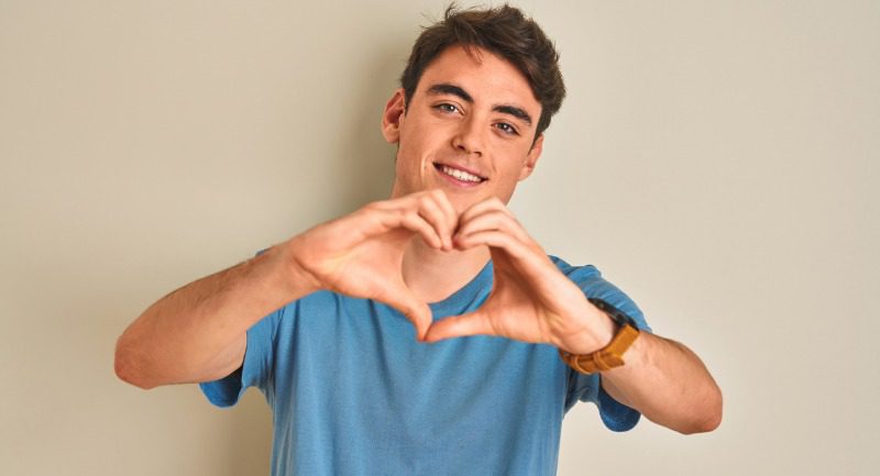 Teenage boy wearing a blue t-shirt making a heart shape with his hands