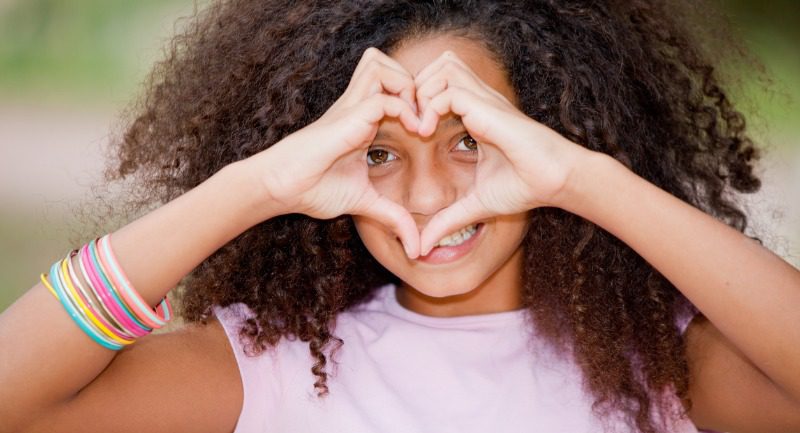 Young girl making a heart shape with her hands and holding it up to her face