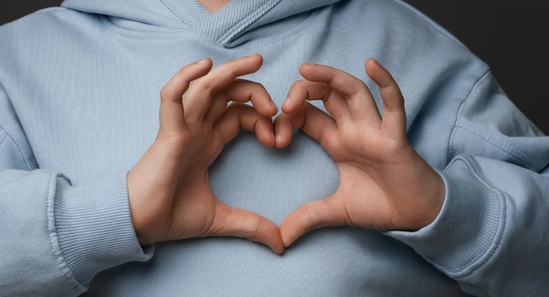 Close up of a boy making a heart gesture with his hands over his chest