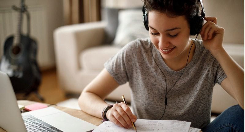Young female student studying while listening to music on headphones