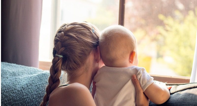 young girl holding up her baby sibling to a window