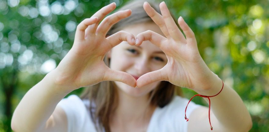 A young teenage girl making a heart shape with her hands and smiling through the gap