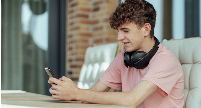 Teenage boy looking at his smartphone with headphones round his neck Teenage boy looking at his smartphone with headphones round his neck