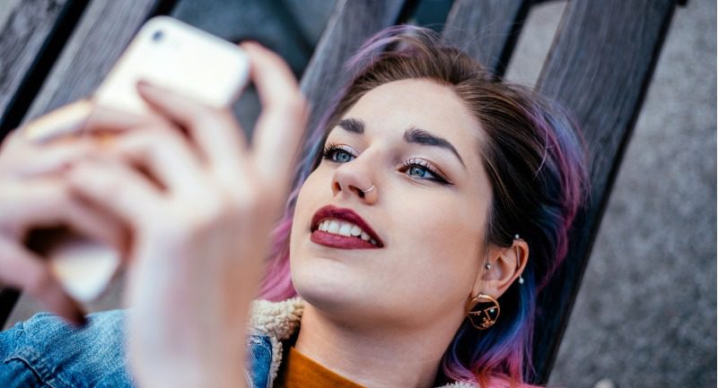 Young woman lying on a bench using her phone