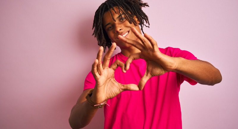 A young man with dreadlocks making a heart shape with his hands