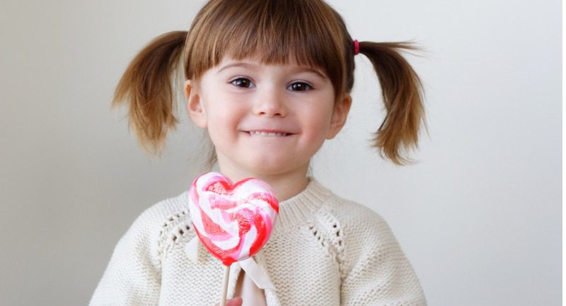 A young girl holding a pink heart shaped lollipop