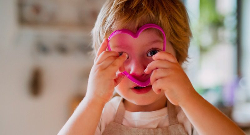 A small toddler boy looking through a heart shaped cake cutter