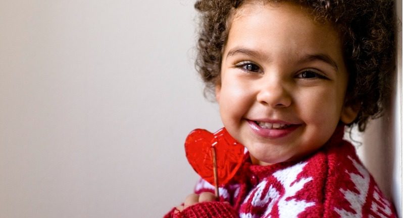 A young happy child holding a heart shaped lollipop