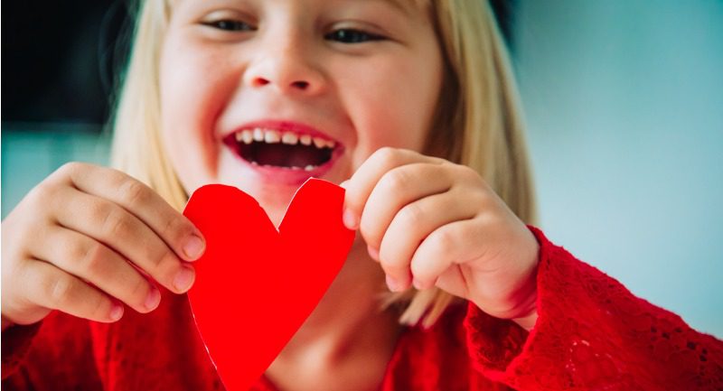 A happy young girl holding a paper heart in her hands