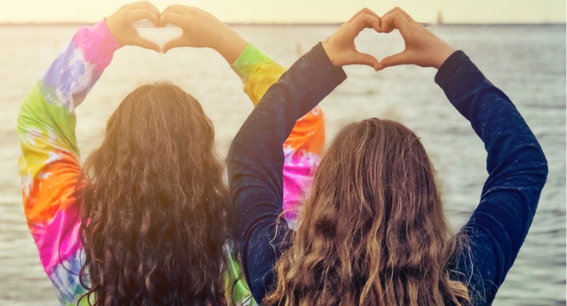 Two young women with their back to the camera making hearts with their hands above their heads