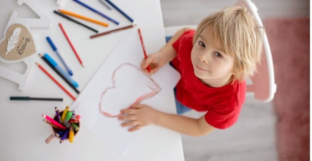 A toodler drawing a picture of a heart in red crayon