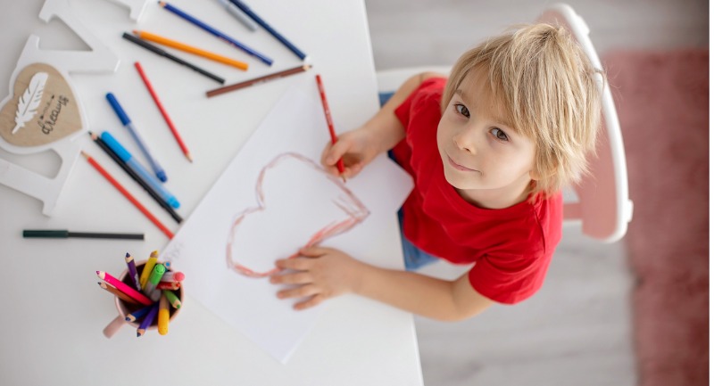 A toodler drawing a picture of a heart in red crayon