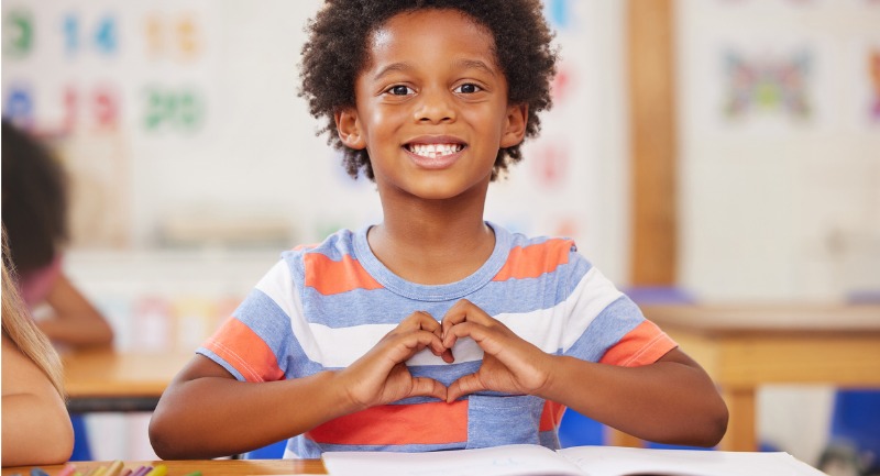 A young boy makes a love heart with his hands