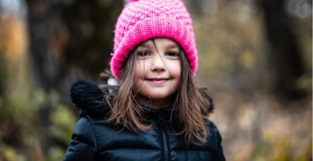 A young girl with shoulder length brown hair wearing a pink beanie hat