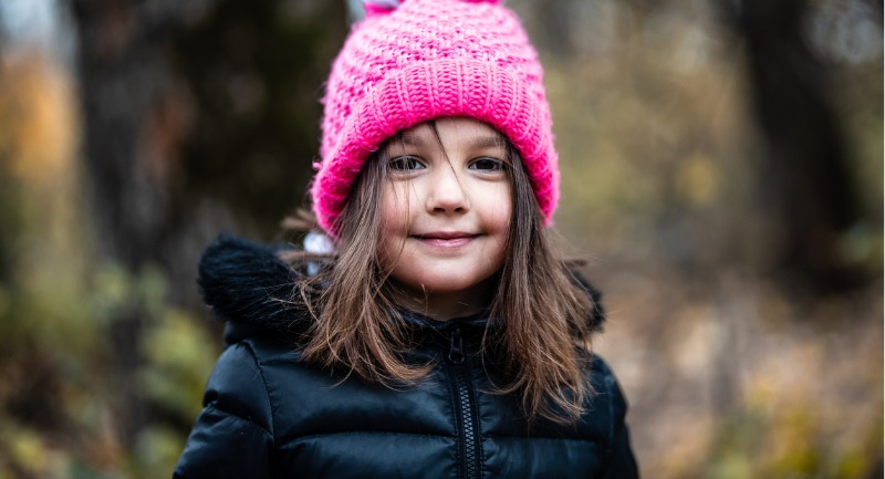 A young girl with shoulder length brown hair wearing a pink beanie hat