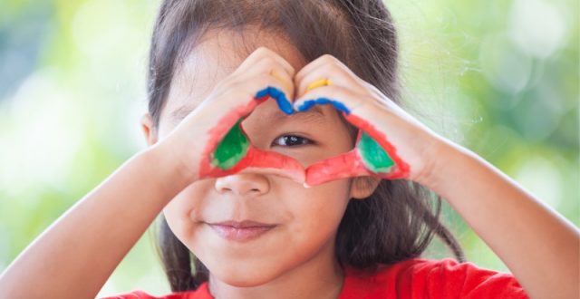 A young girl with pain on her hands makes a love heart gesture with her hands