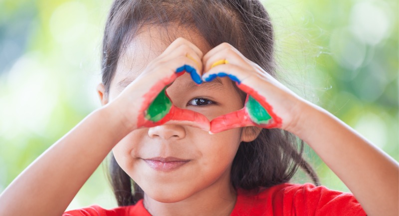 A young girl with pain on her hands makes a love heart gesture with her hands