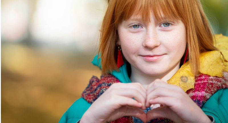 A red haired girl making a love heart with her hands