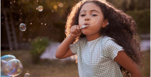 Little girl blowing bubbles with hand-made wand in the garden