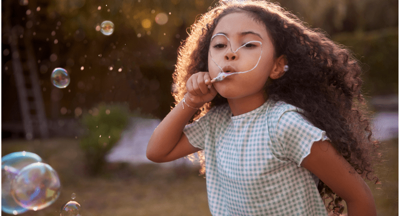 Little girl blowing bubbles with hand-made wand in the garden