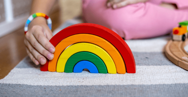 A rainbow toy made of wood being played with by a small child