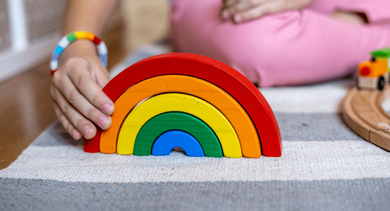 A rainbow toy made of wood being played with by a small child