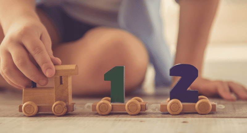 Small child playing with colourful wooden toy train