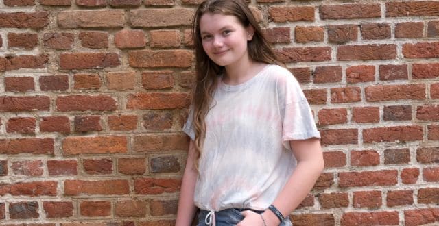Young girl smiling standing in front of a brick wall